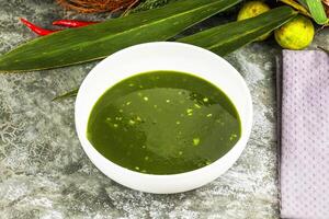 A bowl of green soup with a napkin on a table photo