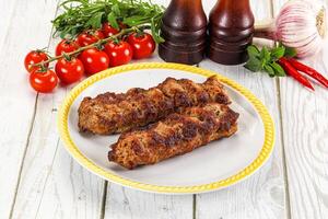 Two meat skewers on a plate with tomatoes and other vegetables photo