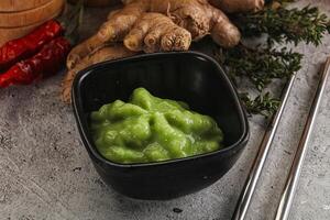 A bowl of green sauce next to some ginger and other ingredients photo