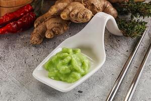 A bowl of green sauce next to a spoon and some ginger photo