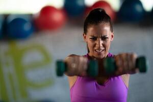 A focused and determined woman performs a strength building dumbbell workout at the gym, showcasing her athletic physique and dedication to fitness. photo
