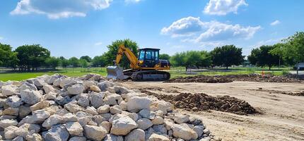 Excavator moves rocks at construction site, sunny day, trees background photo
