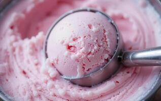 A scoop of pink ice cream is being scooped into a bowl photo