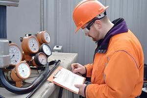 Gas engineer taking readings of pressure gauges and recording data photo