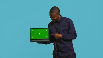 Portrait of happy security guard at work showcasing green screen laptop while overseeing premises. Cheerful private law enforcement worker presenting chroma key notebook, studio backdrop, camera B photo
