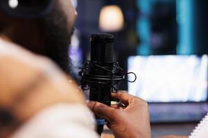 Closeup of african american person with a beard speaking into a microphone creating asmr content. Detailed view of black man using modern audio equipment to create a podcast episode at home. photo