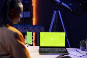 Student at desk using green screen notebook and phone, browsing internet, researching information online. Person i reading articles on chroma key laptop and smartphone for school tasks photo