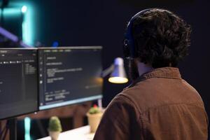 Cybersecurity specialist listening music while looking for company security vulnerabilities, preventing malware infections. Programmer with headphones on preventing cyber attacks on PC photo