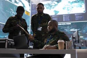 Army personnel collecting real time information and processing details for a new field operation, high tech military command post. Surveillance for a successful defense mission, strategic objectives. photo