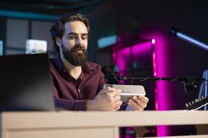 Smiling content creator doing technology review of wireless portable speaker for online platforms channel. Cheerful influencer presenting music playing device to his audience photo