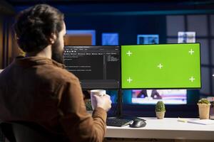 Programmer drinking hot beverage and using green screen PC for futureproofing company network from downtimes and unexpected system failures. Admin with coffee mug in front of mockup computer photo
