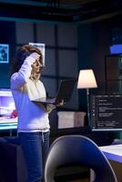 Stressed programmer trying to fix vulnerabilities in software systems using notebook, suffering headache. Tired woman feeling pain from fatigue, using laptop to patch security exposures photo