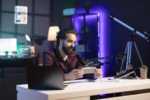 Happy internet star doing technology review of Bluetooth portable speaker for online platforms channel. Smiling influencer presenting music playing device to his viewership photo