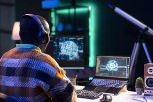 Professional male developer manages neural network at desk, working with AI code on laptop. African american IT expert freelancer developing cyber security, creating secure database. photo