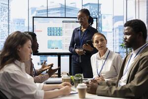 Marketing specialist using monthly infographics on interactive board in a status update meeting, studying numbers and analytics with data reports. Employees team operating smart technology. photo