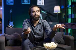 Man disagreeing with characters while watching movie on streaming services, having relaxing evening. Upset viewer in apartment unhappy plot events in film scene, looking dismayed photo