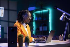 Woman wearing glasses using laptop in home office, checking emails displayed on screen, reading messages in inbox, composing and sending replies, managing electronic correspondence photo