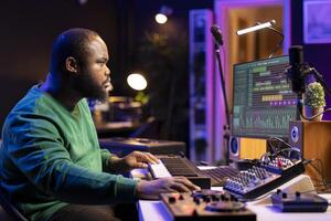 Music engineer producing a song by mixing and mastering tunes on audio console, playing piano notes on synthesizer to record sounds on pc software. Producer creating soundtracks with midi controller. photo