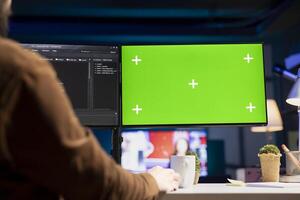 Man does software quality assurance, reading source code on mockup green screen computer before implementing it. Developer inspecting coding on chroma key PC, looking to fix potential issues photo