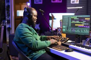 Confident music engineer working on mixing console in home studio, producing new sounds for a song and editing volume levels in daw software. Audio technician recording acoustic files. photo