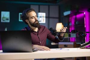 Content creator adjusting professional microphone in studio before starting recording for online vlogging channel. Man in neon lit home studio preparing equipment for vlog shooting photo