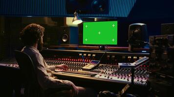 Tracking engineer watching tutorials online to learn mixing and mastering techniques, greenscreen display on pc and processing sounds. Artist technician operates control room switchers. Camera B. photo