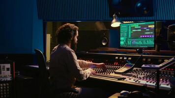Control room sound engineer editing music with sliders and knobs, working on post production in professional soundproof studio. Technician producing songs on stereo mixing console. Camera B. photo