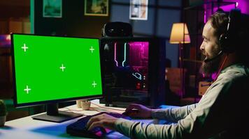 Man having fun by using green screen computer monitor to play singleplayer videogame. Professional gamer using mockup PC desktop to complete levels in game, talking with friends photo