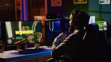 Man happy after finishing videogame, receiving winning message on gaming PC screen in dimly lit apartment. Gamer being victorious after battling enemies in singleplayer shooter photo