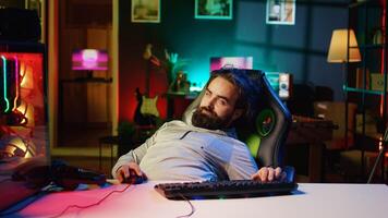 Man obsessed with playing videogames all day falling asleep at computer desk, crushing on floor from tiredness. Gamer suffering from gaming addiction feeling extremely sleepy, dropping from chair photo