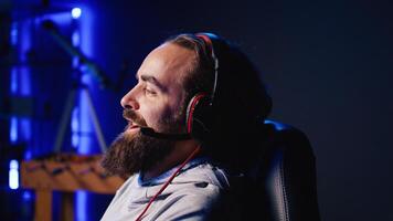 Smiling man plays online multiplayer spaceship videogame with friends, chatting using headphones mic. Panning shot of happy player talking with teammates, flying spacecraft, enjoying leisure time photo
