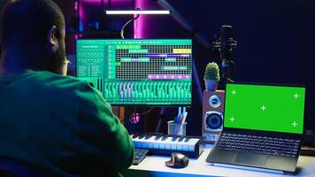 Music producer mixing and mastering songs on digital post production pc interface, green screen display. Artist adding sound effects and adjusting volume levels to produce new music. Camera B. photo