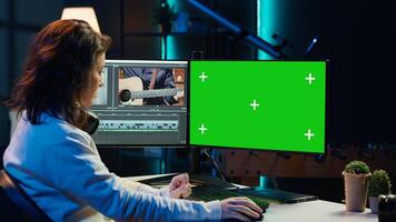 Videographer uses editing software on chroma key computer to assemble footage into final product. Woman color correcting clips on isolated screen PC to ensure project meets desired aesthetic, camera A photo
