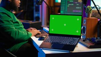 Professional artist operating on daw software in home studio, using a green screen layout next to him. Producer editing his audio recordings by applying mixing and mastering techniques. Camera A. photo