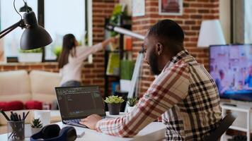 African american software developer works on programming code on a laptop in remote workspace. Productive IT engineer working on coding, software design and internet security innovation. Camera B. photo