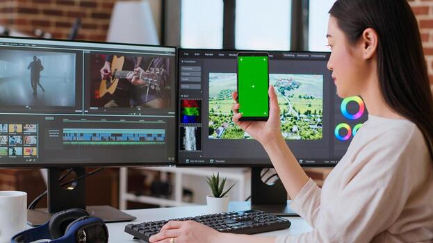 Professional asian woman working on a media project next to green screen in a modern space, using dual monitors and advanced editing software. Multitasking in post production. Camera A. photo