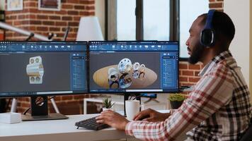 African american industrial designer works on CAD software and listens to music, multitasking at home. Engineer specialist uses digital tools and 3D modeling for industrial projects. Camera B. photo
