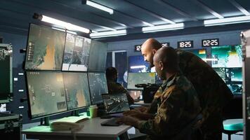 Military soldier in mission control center, overseeing national safety operations using notebook next to colleague. Team of army specialists examining data in monitoring room command center, camera B photo
