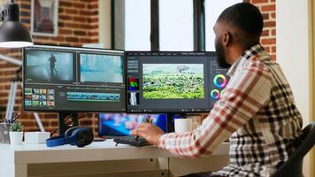 African american man editor working in production industry, does color grading and editing a film project on dual monitors. Showing the creative process with tech tools. Camera B. photo