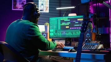 Producer composing new music on acoustic instrument in home studio, using microphone to sing chords. Musician songwriter works with mixing console and software, guitarist producing tunes. Camera A. photo