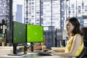 Company worker sitting at desk in office, doing research for team project on green screen PC. Woman looking at mockup computer in modern relaxed workplace solving tasks during job shift photo