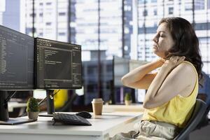 Developer suffering neck pain while fixing applications issues, dealing with databases and server configuration. Fatigued woman feeling overworked while optimizing company software photo