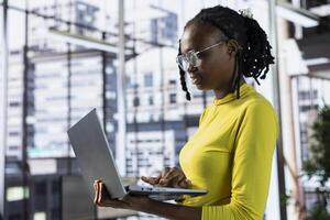 Worker standing in office using laptop during job shift, looking through online financial business documents. Company employee in workspace doing tasks on notebook, being productive photo