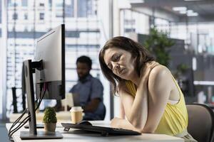 Worker in office feeling shoulder during job shift, feeling overworked while looking through online business documents. Fatigued company employee suffering injury in workspace while doing tasks photo