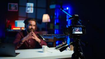 Focus on professional camera used by man in blurry background hosting online show in neon lit studio. Close up of high tech gear used by vlogger during streaming service broadcast, camera B photo