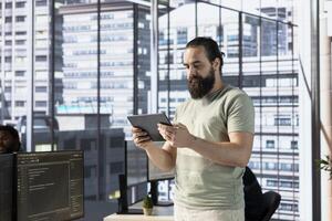 Programmer creating machine learning models that can process and analyze data to improve and automate decision making processes, looking at tablet. Man programming in office using device photo