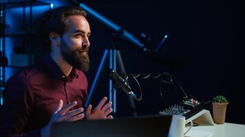 Upbeat content creator hosting online show in rgb lights studio, shooting vlog using professional microphone. Cheerful vlogger presenting informations during streaming service broadcast, camera B photo