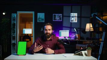 Happy influencer in studio filming chroma key tablet review for tech enthusiasts. Joyful media star hosts technology internet show, unboxing isolated screen digital portable device, camera B photo