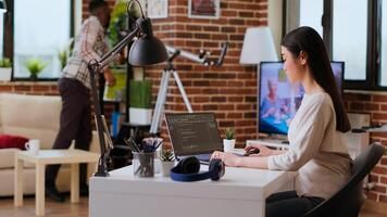 Software developer types programming code in a cozy home office setup. Asian woman coding for cloud computing on her laptop, enhances productivity for software development. Camera B. photo