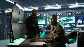 Intelligence operative in military base doing surveillance with digital radar equipment, operating missile systems. African american man monitoring army HQ CCTV for any unauthorized activity, camera B photo